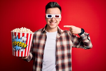 Wall Mural - Young handsome caucasian man wearing 3d movie glasses and eating popcorn smiling cheerful showing and pointing with fingers teeth and mouth. Dental health concept.