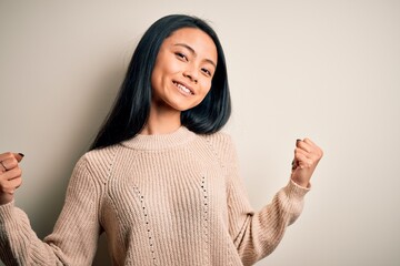 Wall Mural - Young beautiful chinese woman wearing casual sweater over isolated white background very happy and excited doing winner gesture with arms raised, smiling and screaming for success. Celebration