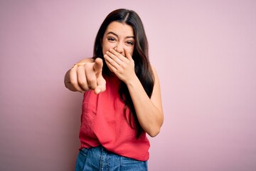 Young brunette woman wearing casual summer shirt over pink isolated background laughing at you, pointing finger to the camera with hand over mouth, shame expression