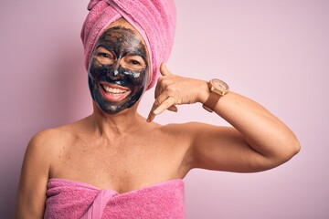 Wall Mural - Middle age brunette woman wearing beauty black face mask over isolated pink background smiling doing phone gesture with hand and fingers like talking on the telephone. Communicating concepts.