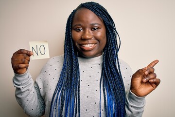 Sticker - Young african american plus size woman with braids holding reminder paper with no message very happy pointing with hand and finger to the side