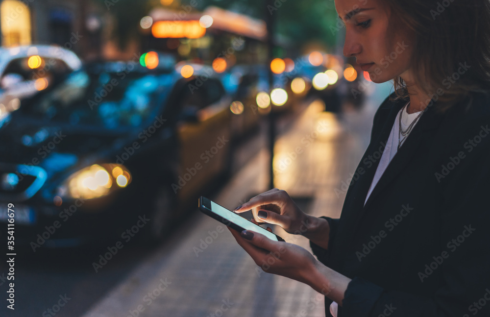 Elegant woman pointing on screen smartphone background headlights auto in night city street, tourist girl using internet technology calls a taxi standing next to the road in busy street of evening - obrazy, fototapety, plakaty 