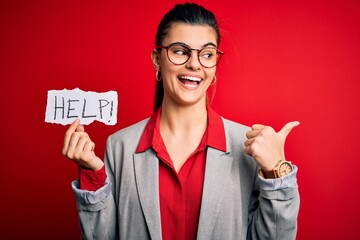 Young beautiful brunette businesswoman with problems holding paper with help message pointing and showing with thumb up to the side with happy face smiling