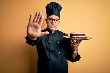 Poster - Middle age handsome grey-haired baker man wearing cooker uniform and hat holding cake with open hand doing stop sign with serious and confident expression, defense gesture