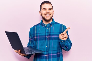 Young handsome man working using laptop smiling happy pointing with hand and finger to the side