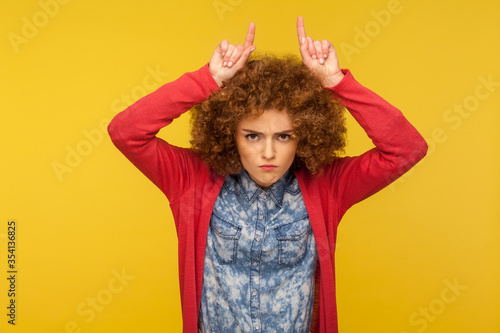 Fotomural Do you want problems? Portrait of angry curly-haired woman showing bull horn gesture and threatening to attack, metaphor of intimidation, aggressive behavior