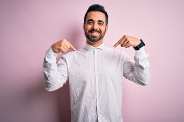 Young handsome man with beard wearing casual shirt standing over pink background looking confident with smile on face, pointing oneself with fingers proud and happy.