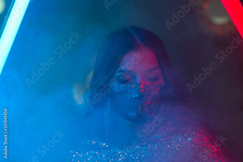 Woman wearing stylish sequin face mask posing, dancing in colorful bright neon uv blue and red lights Tableau sur Toile