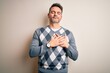 © Krakenimages.com - Young handsome man wearing casual sweater standing over isolated white background smiling with hands on chest with closed eyes and grateful gesture on face. Health concept.