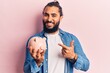 © Krakenimages.com - Young arab man holding piggy bank smiling happy pointing with hand and finger