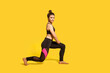 © khosrork - Athletic slim young woman with hair bun in tight sportswear doing sport lunge exercise, standing one knee, warming up training muscles, butts workout. full length studio shot, isolated on yellow