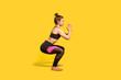 © khosrork - Athletic woman with hair bun in tight sportswear doing squat, lower body sport exercise, keeping balance, warming up and training muscles. full length studio shot, isolated on yellow background
