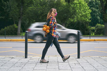 Young Woman Wearing A Plaid Handmade Face Mask And Colorful Shirt With Mesh Bag Full Of Oranges Walking On The Street On Passing Car Background. Zero Waste Concept.