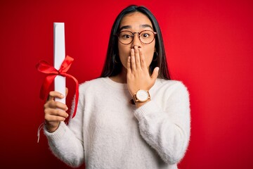 Sticker - Young beautiful graduate asian woman holding university degree diploma over red background cover mouth with hand shocked with shame for mistake, expression of fear, scared in silence, secret concept