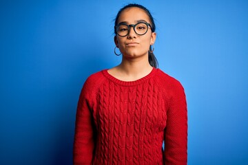 Young beautiful asian woman wearing casual sweater and glasses over blue background Relaxed with serious expression on face. Simple and natural looking at the camera.