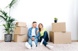 Relocation into new home. Happy guy and girl loving each other moving in a new home, they are sitting on the floor in casual wear and hugging among cardboard boxes
