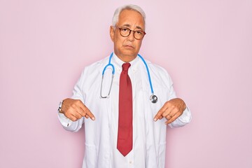 Canvas Print - Middle age senior grey-haired doctor man wearing stethoscope and professional medical coat Pointing down looking sad and upset, indicating direction with fingers, unhappy and depressed.