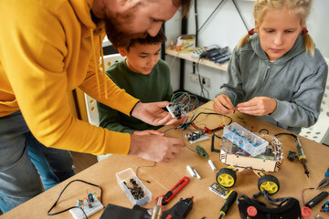 Making it happen. Cropped shot of young technicians building a robot, working with a wiring kit together with a male teacher at a stem robotics class. Inventions and creativity for kids