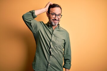 middle age hoary man wearing casual green shirt and glasses over isolated yellow background confuse 