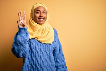 Wall Mural - Young African American afro woman wearing muslim hijab over isolated yellow background showing and pointing up with fingers number three while smiling confident and happy.