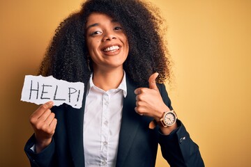 Young african american business woman with afro hair holding help paper for work stress happy with big smile doing ok sign, thumb up with fingers, excellent sign