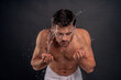 Handsome young man isolated. Portrait of shirtless muscular man is standing on grey background and washing oneself. Spraying water into face. Men care concept.