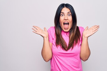 Poster - Young beautiful brunette woman wearing casual pink t-shirt standing over white background celebrating crazy and amazed for success with arms raised and open eyes screaming excited. Winner concept