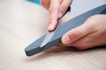 Strong male hands sharpen a kitchen metal knife with a grindstone. Home household knife sharpening.