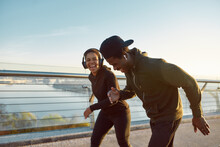 Enjoying Run. Side View Of Happy Young African Couple, Man And Woman In Headphones Laughing While Running On The Bridge In The Early Morning