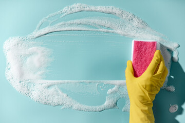 Hand in a yellow rubber glove holds a cleaning sponge and wipes a soapy foam on a blue background. Cleaning concept, cleaning service