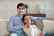 © fizkes - Portrait of smiling young man and woman sit relax n sofa at home hugging and cuddling, happy millennial caucasian couple rest on couch embracing, enjoy tender romantic weekend indoors together