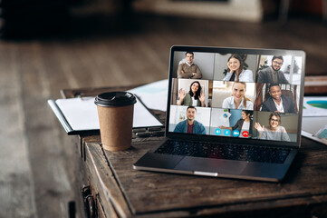 Wall Mural - Virtual meeting online. Video conference by laptop. Online business meeting. On the laptop screen, people who gathered in a video conference to work on-line, near stands a cup of coffee