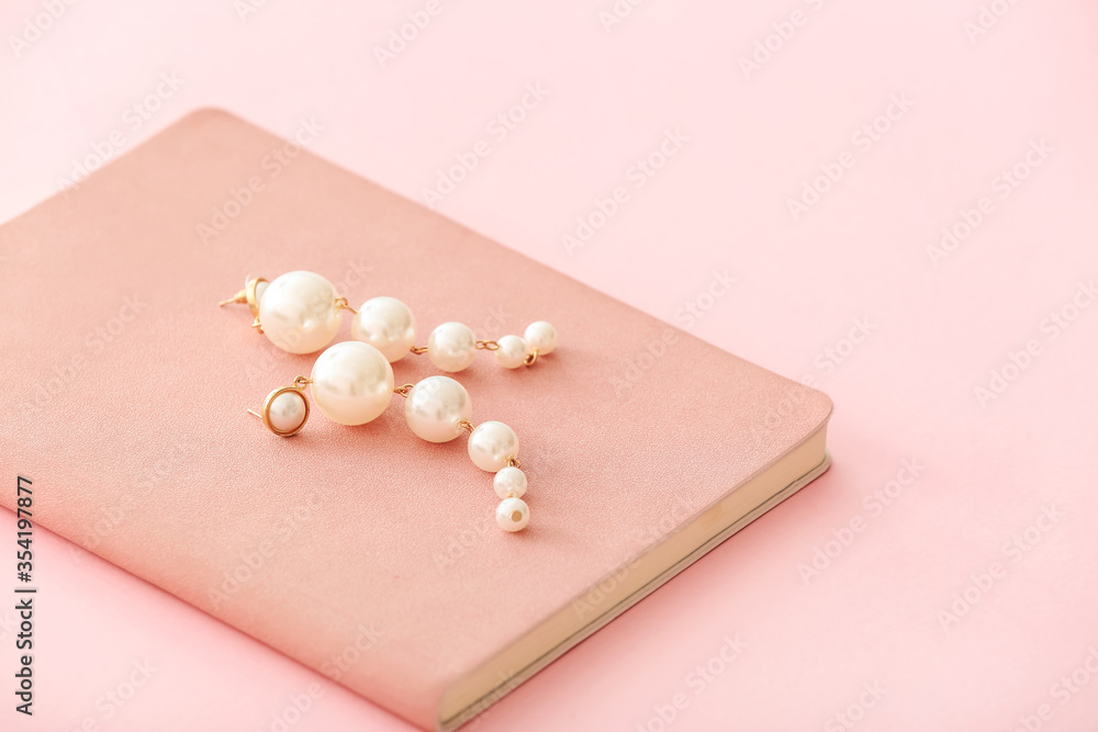Beautiful earrings with notebook on color background