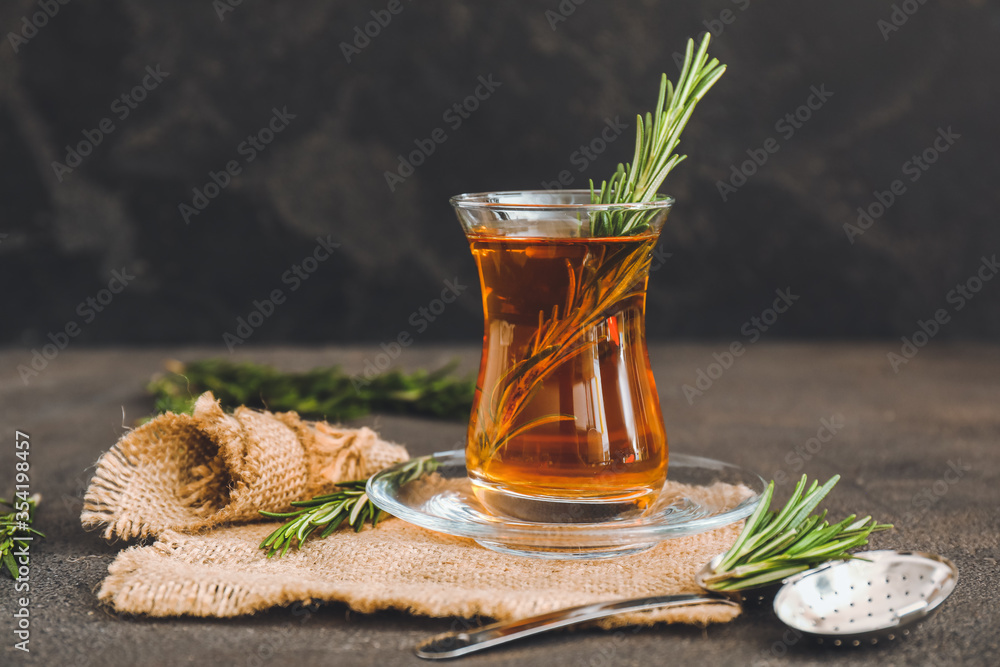 Cup of hot tea with rosemary on dark background