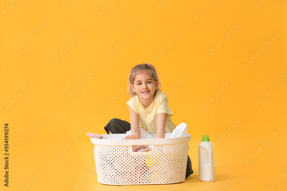 Little girl with laundry on color background