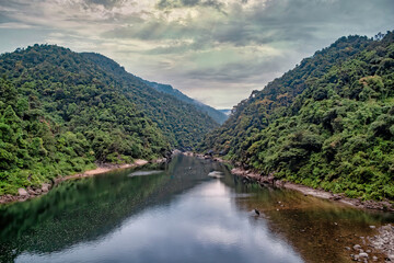 The Umngot River, Meghalaya, India – October 13, 2018 – A lone fishing boat crosses the crystal clear green waters of the Umngot River flowing past the Shnongpdeng village