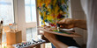 © Prathankarnpap - Cropped image of artist hands while holding and mixing oil color on artist palette over painting canvas and comfortable sitting room windows as background.