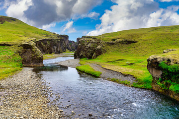 Wall Mural - Amazing view at Fjadrargljufur Canyon is a deep canyon in the south-eastern part of Iceland. The Fjaðrá River flows through steep walls and meandering water, in summer with green grass and blue skies.