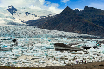 Sticker - Group of tourists are standing and looking at the amazing views of the Fjallsarlon mountains and lakes with large glaciers and icebergs floating in the water in Vatnajokull National Park in Iceland.