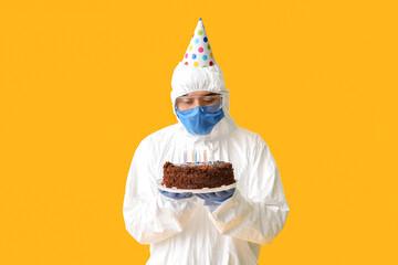 Canvas Print - Asian man in biohazard suit and with Birthday cake on color background. Concept of epidemic