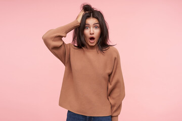 Wall Mural - Indoor photo of shocked young brown haired woman raising amazedly her eyebrows while looking dazedly at camera, standing over pink background in casual wear