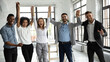 © fizkes - Excited diverse business people celebrating success, holding raised hands, looking at camera, smiling overjoyed employees team rejoicing achievement, laughing and screaming with joy in office room