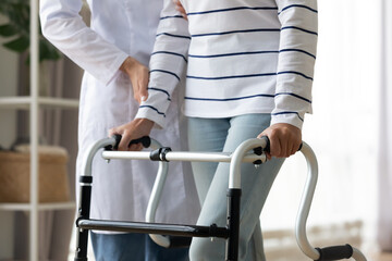 Wall Mural - Cropped image caregiver helping to disabled patient walking with rollator equipment reduce load and joint pain with arthritis. Physical therapist and therapy, neurological cerebellar disorders concept