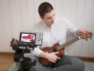 The girl is recording the lesson on a video camera. Broadcast the lesson. Online learning to play the guitar, ukulele. The girl sings and plays the guitar.