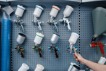 Male worker holds pneumatic paint gun, tool store