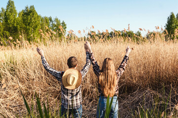 A couple in love in the field. Back view and hands up, sunset light.