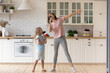 Funny young mom or nanny play sing entertain using kitchen appliances with little preschooler girl child, smiling overjoyed mother have fun enjoy family leisure weekend with small daughter at home
