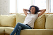© fizkes - Peaceful African young woman resting leaned on comfy couch in modern living room with air-conditioner. Enjoy fresh air at summer day, relaxing alone relish lazy day. No stress fatigue relief concept