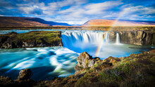 dynamic longtime exposure wide angle panorama of magical godafoss waterfall with romantic rainbow and hills in the background nearby fossholl in iceland