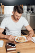 © LIGHTFIELD STUDIOS - Selective focus of man eating noodles near smartphone on books on kitchen table